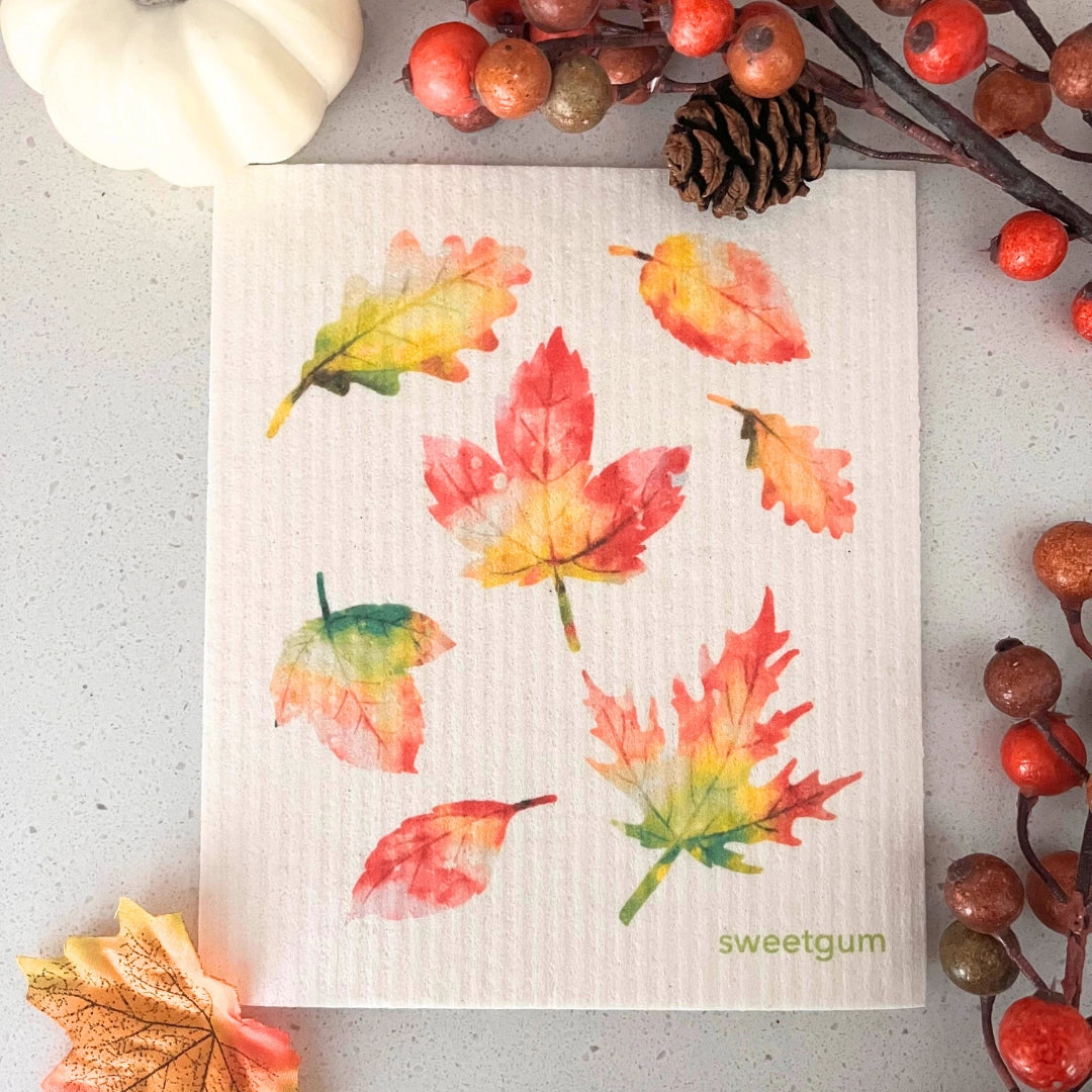 Decorative dishcloth towel with autumn leaf pattern on a gray surface with decorative elements.