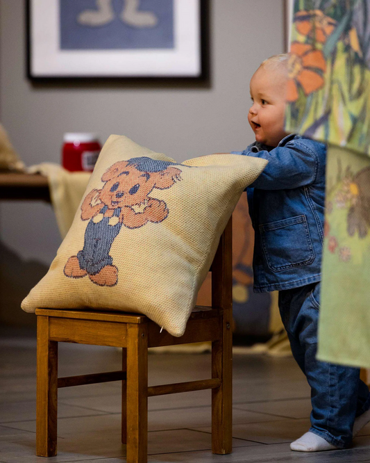 Child playing with a pillow featuring a teddy bear design in a room setting.