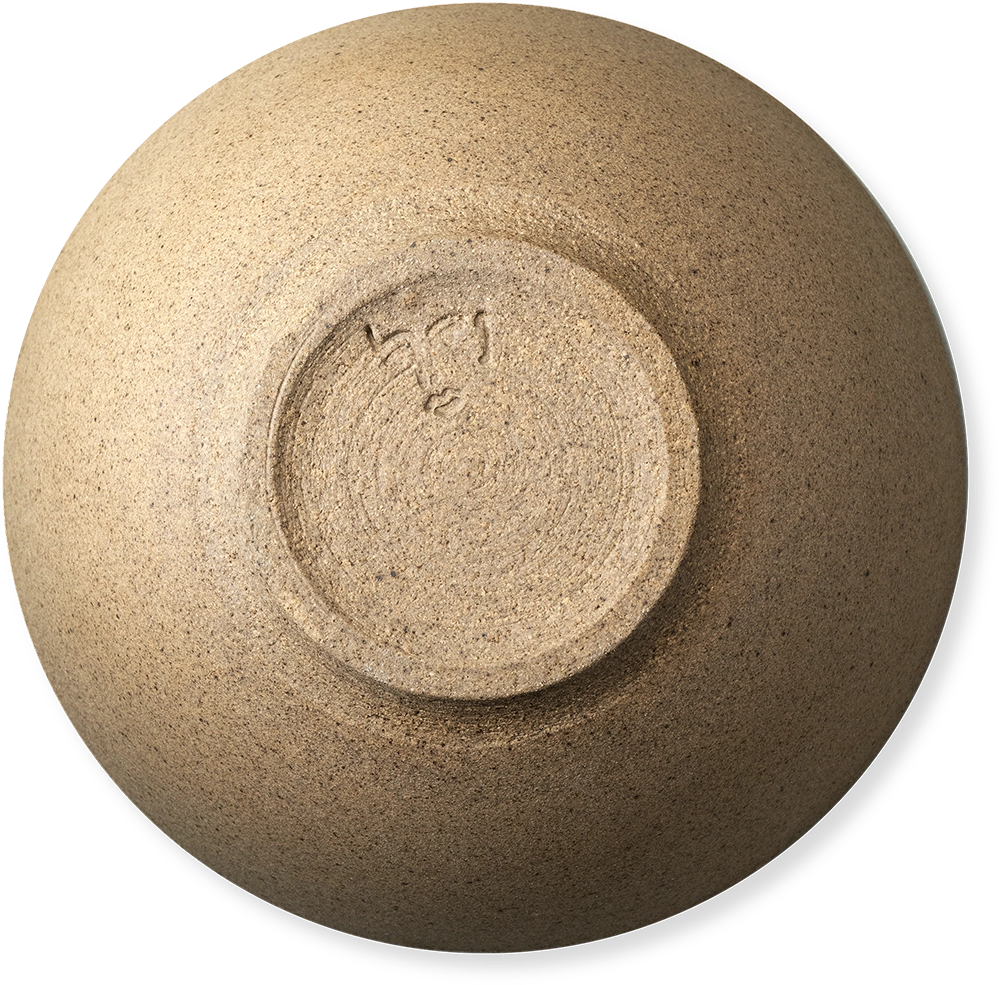 A top-down view of a ceramic bowl with a textured, speckled beige and brown glaze, showing a circular foot ring with a hand-painted signature in the center.