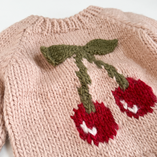 Add a pop of cherry red with this blush pullover features a pair of cherries with knitted appliqué 3-D leaves in a cozy moss color. The design is perfect for the first day of school or a night time walk. The way it looks hanging on a hangar also makes this such a cute piece of decor to hang in your child's room.