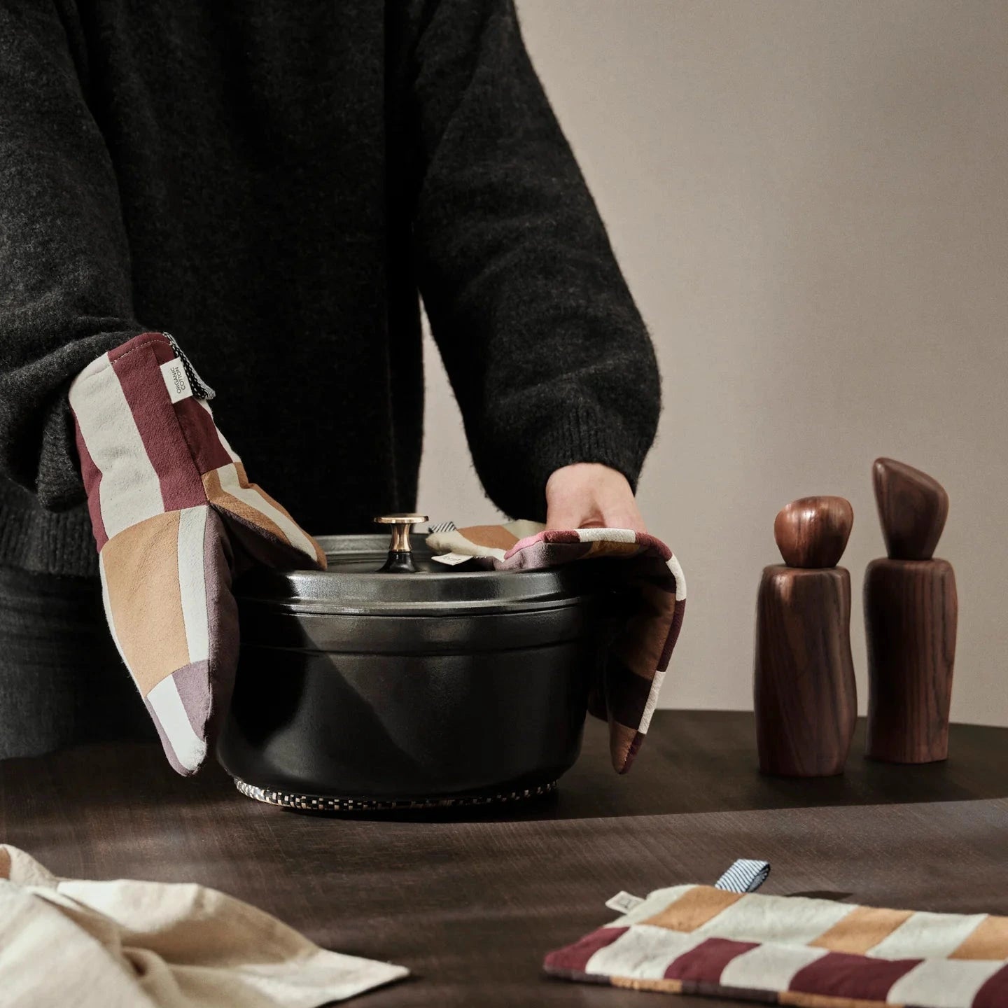 Person holding a black pot with wooden salt and pepper shakers but they use the term living section oven mitt.