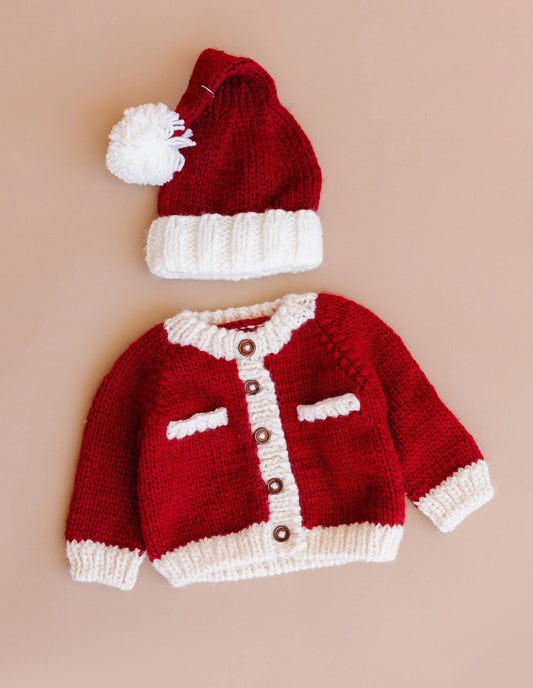 Red knitted baby sweater and hat set on a beige background