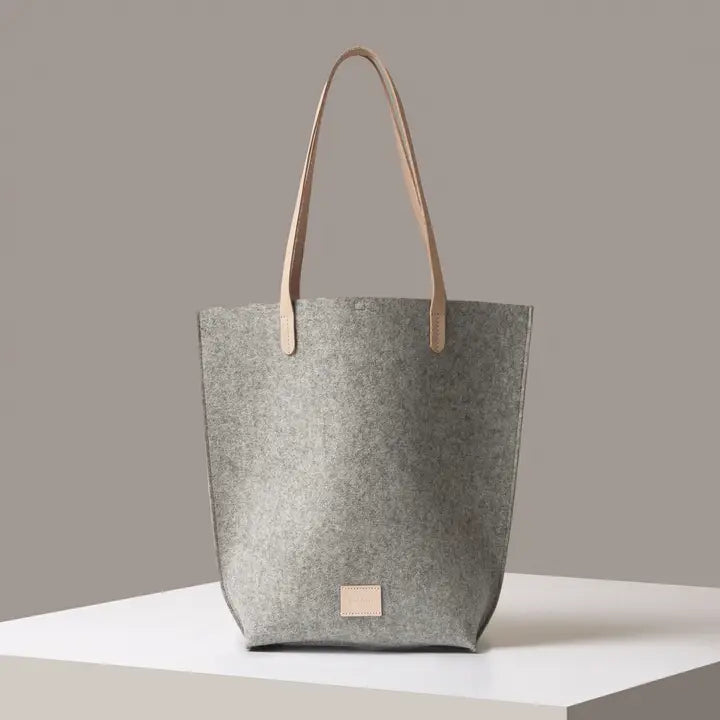 A gray Merino wool felt tote bag with two handles, a front pocket, and vegetable-tanned leather straps.