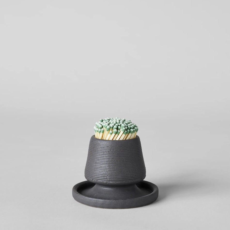 Black ceramic match holder with matches on a gray background. Handmade in the United States and looks lovely as a decorative item. Sold at Huset Shop on Abbot Kinney.