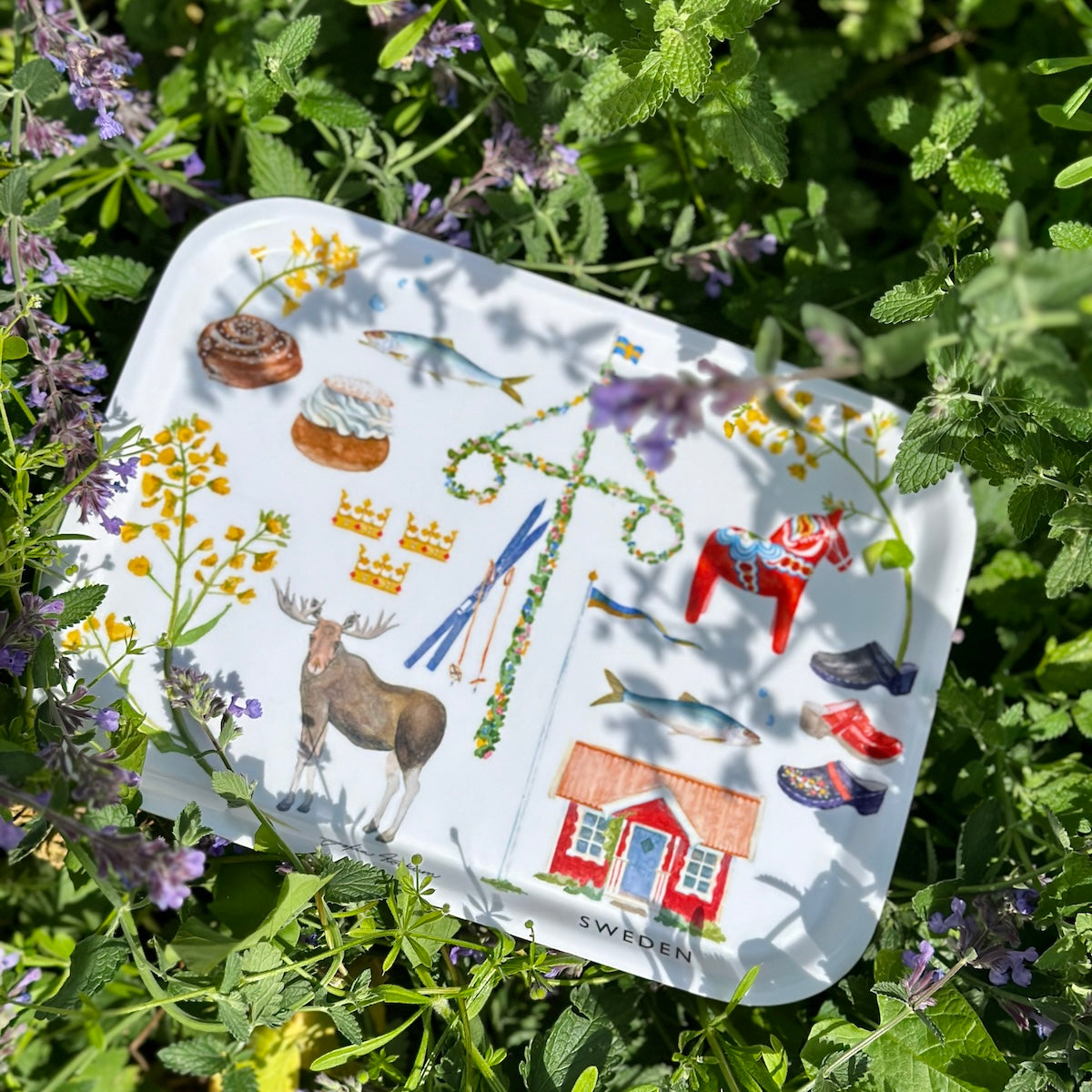 Tray with classic Swedish motifs painted by Sofia Kockum in a lush field of flowers with purple flowers and green leaves.