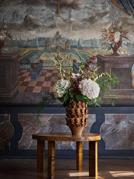 The Terra vase is made from porcelain clay and showcases genuine craftsmanship. The vase is first cast in a mould, after which all details are applied by hand, making each piece unique. It is finished with a matte glaze, also applied by hand. The interior is treated to hold water, but as the clay is naturally porous, some moisture may seep through. Therefore, avoid placing it on delicate surfaces.