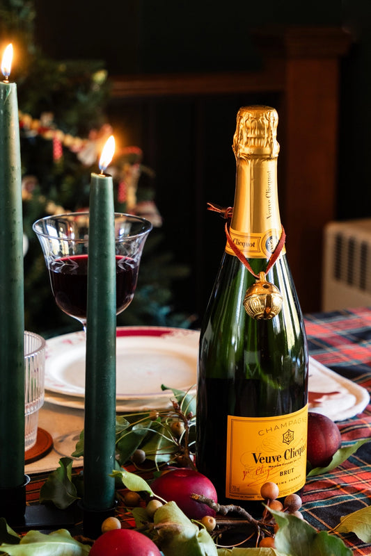 This merry Christmas bell adds holiday cheer no matter how you choose to display it. Beautiful as a tree ornament, it can also be hung on a door handle or tied on a gift as a thoughtful addition to wrapping. Here it is hung around a bottle of Veuve Clicque Champagne.