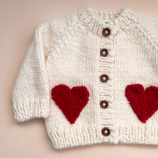 White knitted cardigan with red heart patterns on a beige background