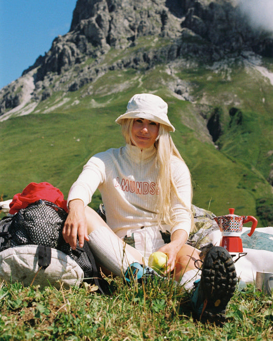 Person sitting in a mountainous area with a scenic background, Amundsen Sports a base layer for skiing or hiking.