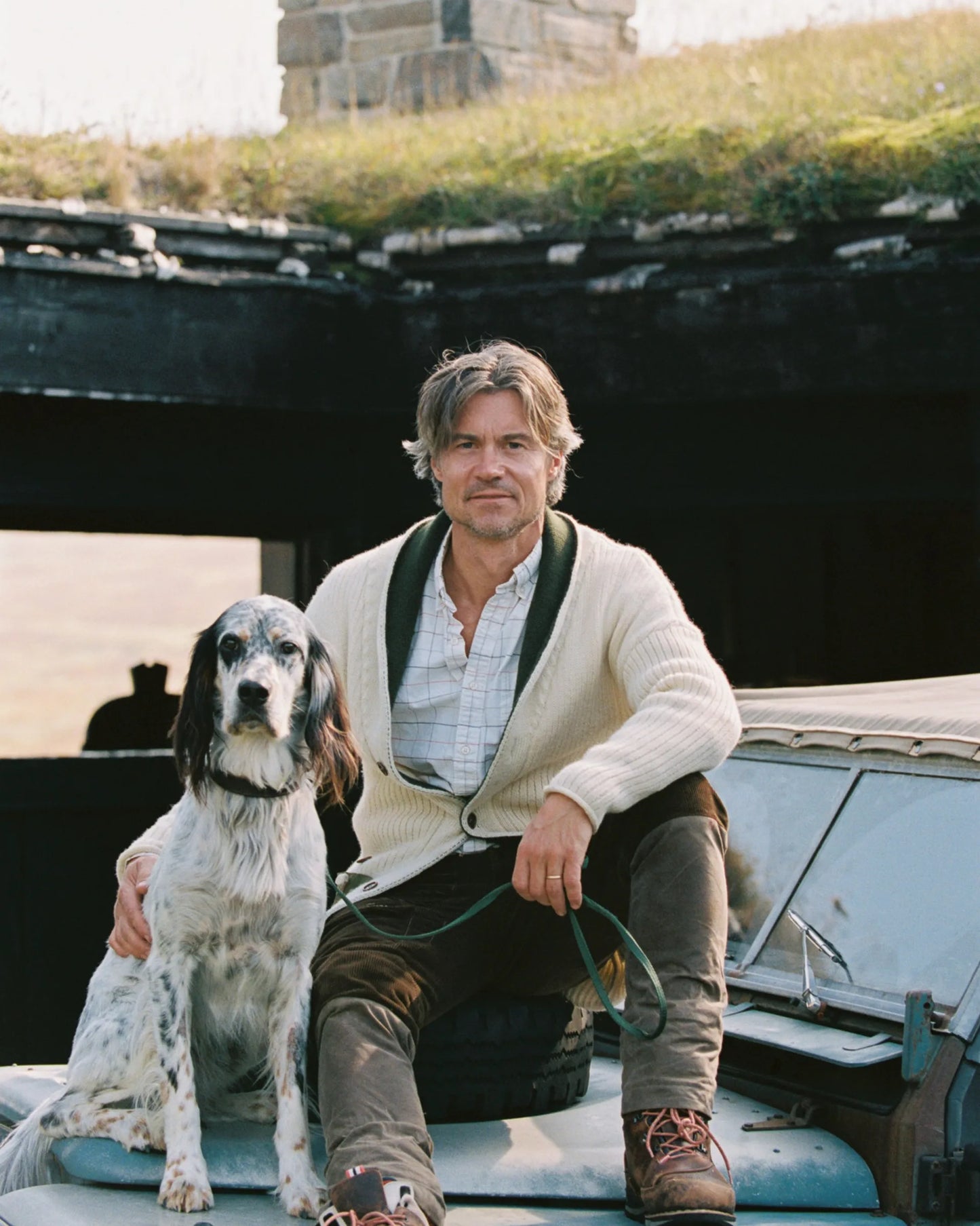 Handsome man in a the new norwegian brand sweater and cardigan standing next to a dog on an old Land Rover in a rustic setting. The cozy nature of this sweater is perfect for fall 2025 and men's fashion. Amundsen Sports, scandinavian, los angeles, venice beach, Huset shop, gift shop and shopping for men and women, dogs, and kids