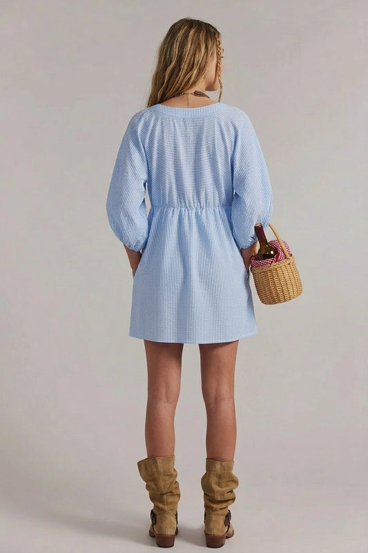Woman wearing a light blue dress holding a woven basket against a plain background