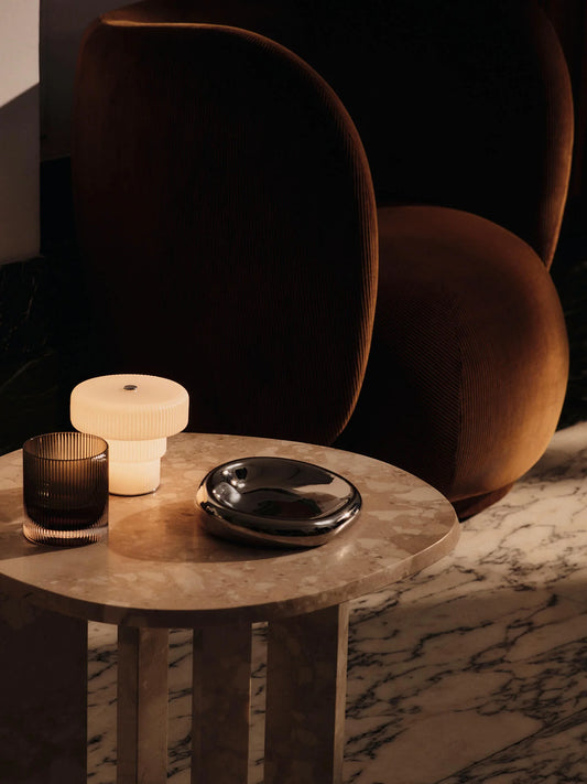 Add a soft glow to your space with the Ripple Portable Lamp. Crafted from mouth-blown glass with a rippled surface and white opal finish, it casts a warm, diffused light. With three brightness levels, the compact design is perfect for intimate evenings or adding ambience to a table setting.