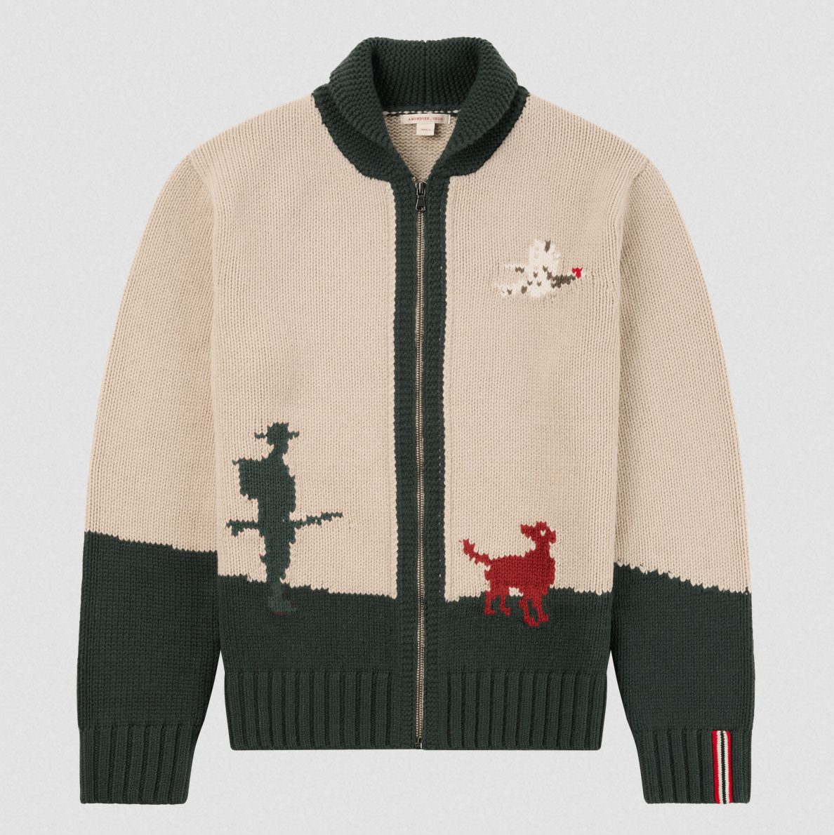 A beige and dark green knit zip-up cardigan sweater with a high ribbed collar, featuring a cowboy silhouette, a red dog, and a white dog graphic on the front, shown against a light gray background.