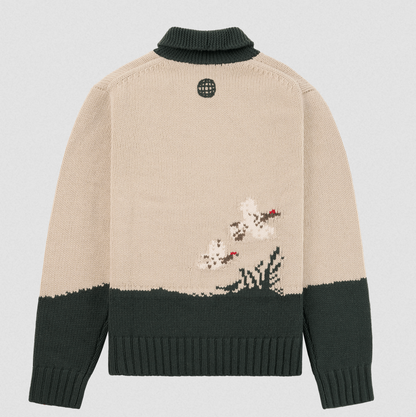 A beige and dark green knit sweater shown from the back, featuring a pixelated floral motif in white, green, and red near the lower back, with a dark green turtleneck collar and ribbed cuffs and hem.
