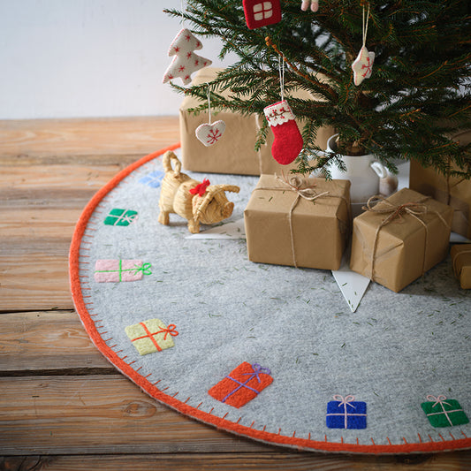 Christmas tree with wrapped gifts and decorations on a tree skirt with colorful presents design. Give your Christmas tree a cozy, festive base with our round x-mas mat, made from soft, sustainable wool to catch needles and add natural charm.