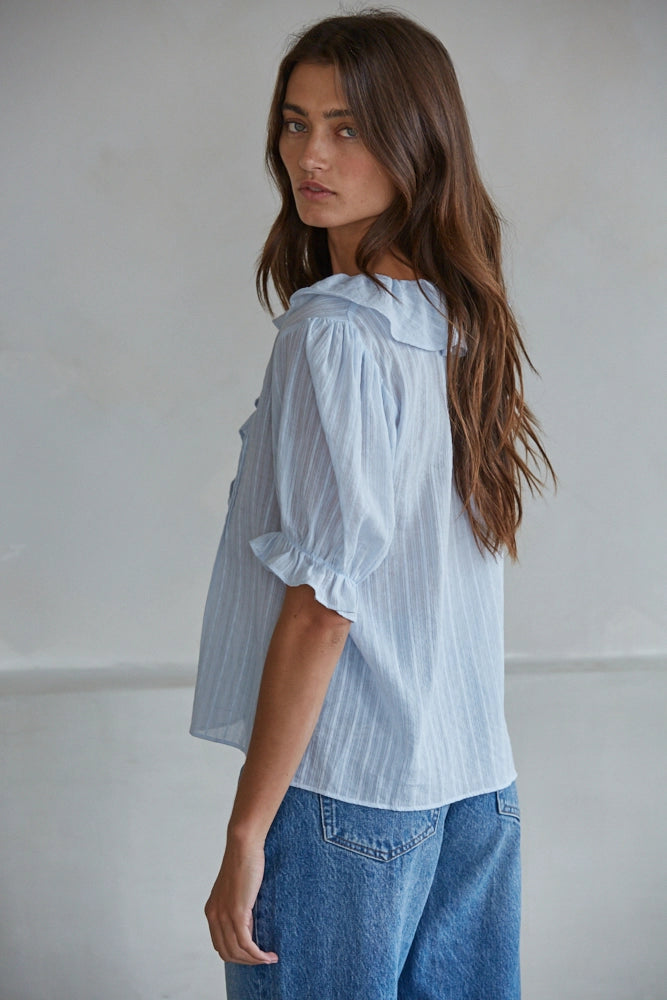 Woman wearing a light blue striped shirt and blue jeans against a plain background