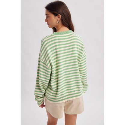 Woman wearing a green and white striped sweater and beige shorts on a plain background