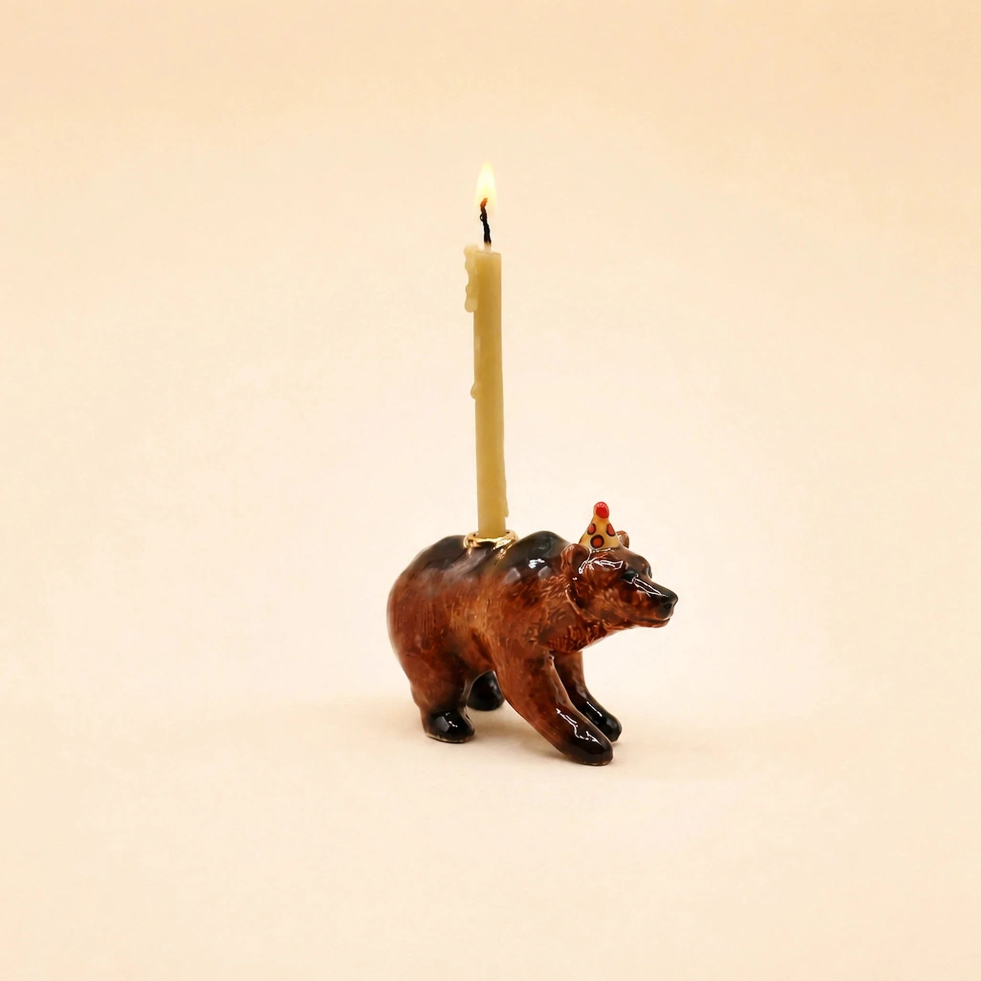 A bear-shaped candle holder with a lit cream-colored candle inserted into its back, set against a solid light beige background.