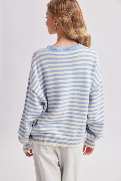 A woman shown from the back wearing a light blue and white horizontally striped knit sweater, paired with light gray sweatpants, against a plain light gray studio background.