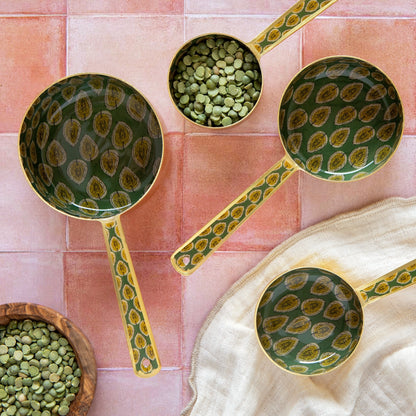 Three green ceramic ladles with gold patterns on a pink tiled background