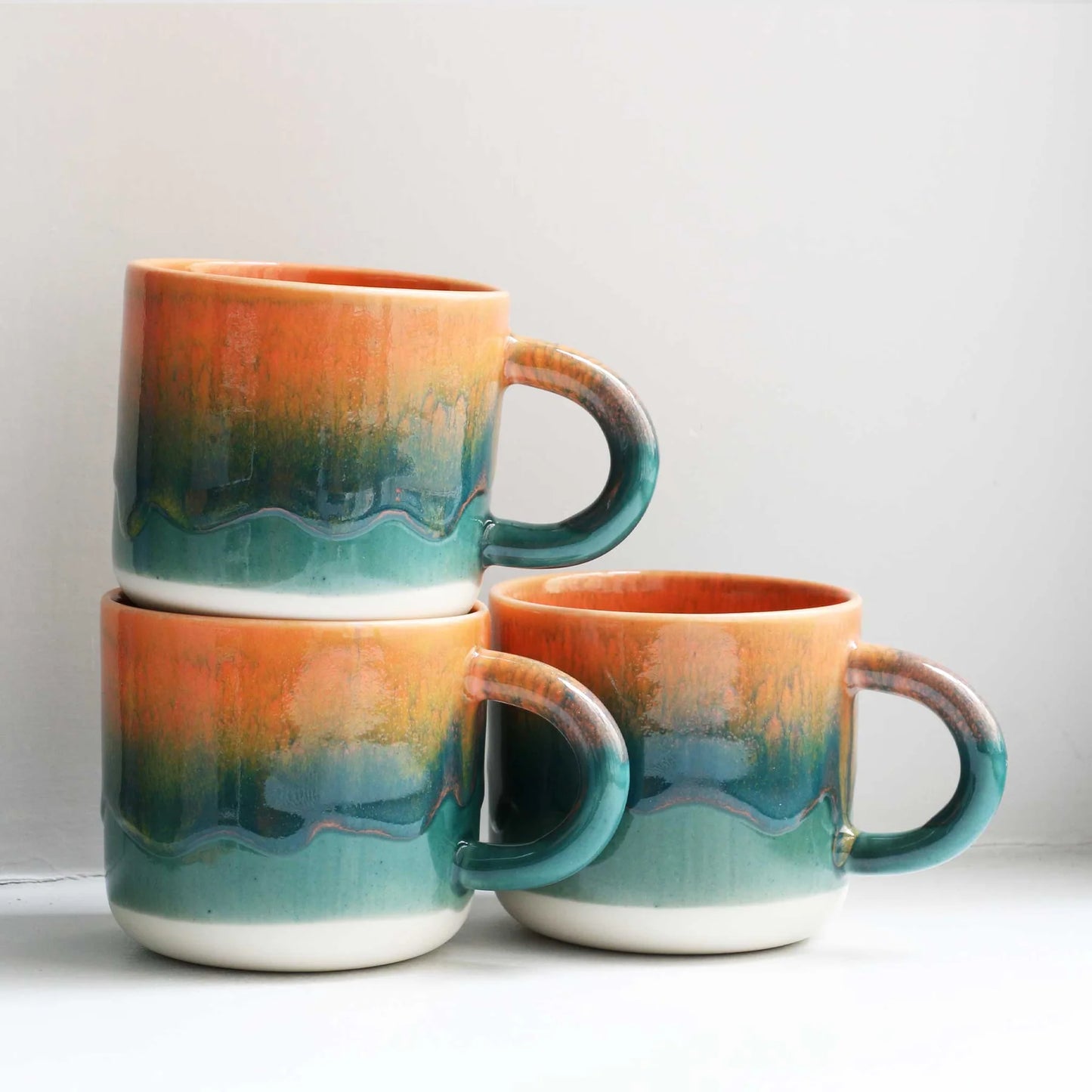 Three ceramic mugs with gradient colors stacked on a light surface.