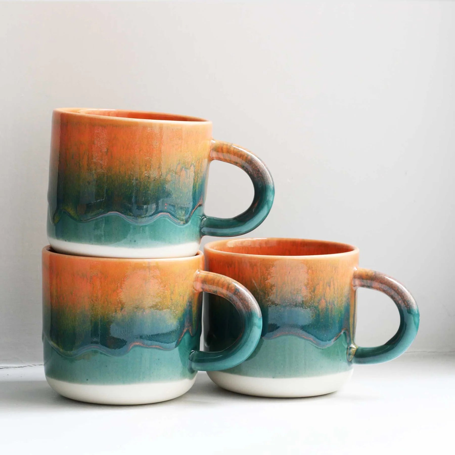 Three ceramic mugs with gradient colors stacked on a light surface.