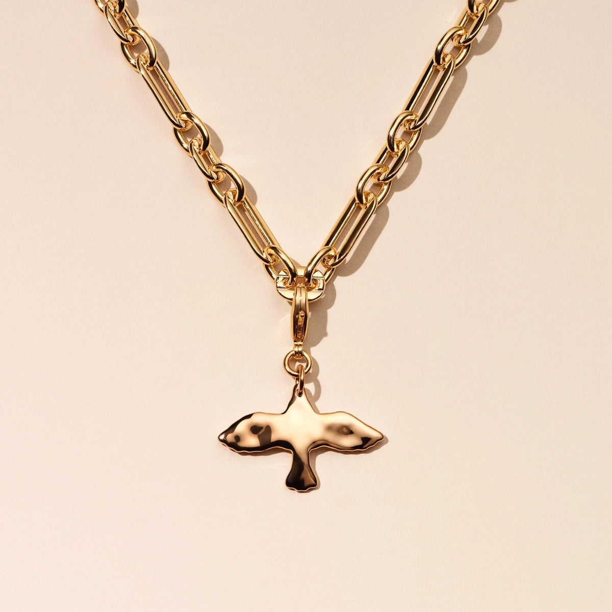 Gold chain necklace with a dove-shaped pendant on a beige background