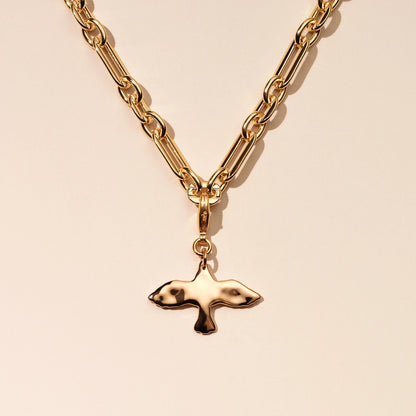Gold chain necklace with a dove-shaped pendant on a beige background