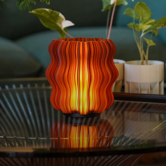 Wavy-patterned orange lamp on a reflective surface with blurred plants in the background