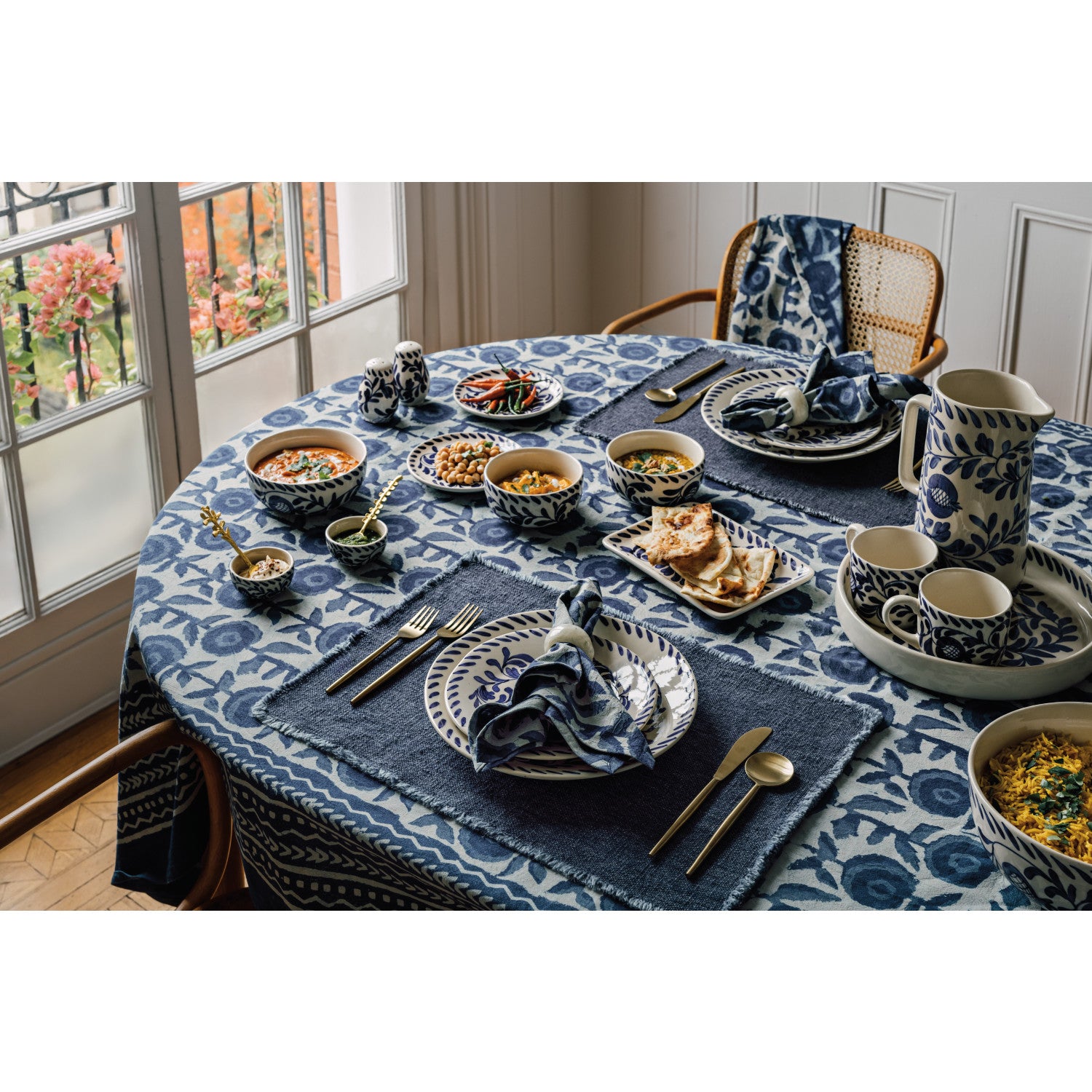 Dining table set with blue and white patterned tablecloth, plates, bowls, and cutlery.