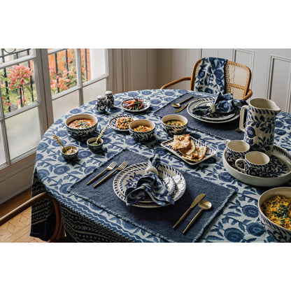 Dining table set with blue and white patterned tablecloth, plates, bowls, and cutlery.