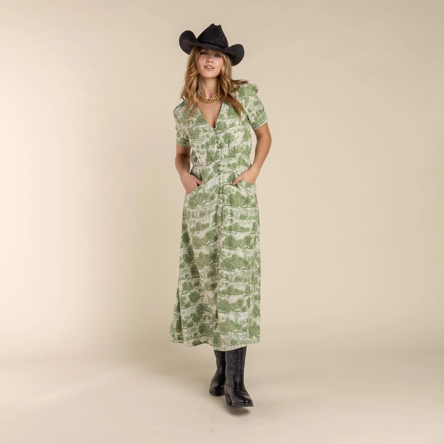 Woman in a green dress holding a black hat against a desert landscape, Woman wearing a green patterned dress and black cowboy hat and the Darcy Dress with feminine charm and a hint of retro style. Stylish dress cowboy rancher girl