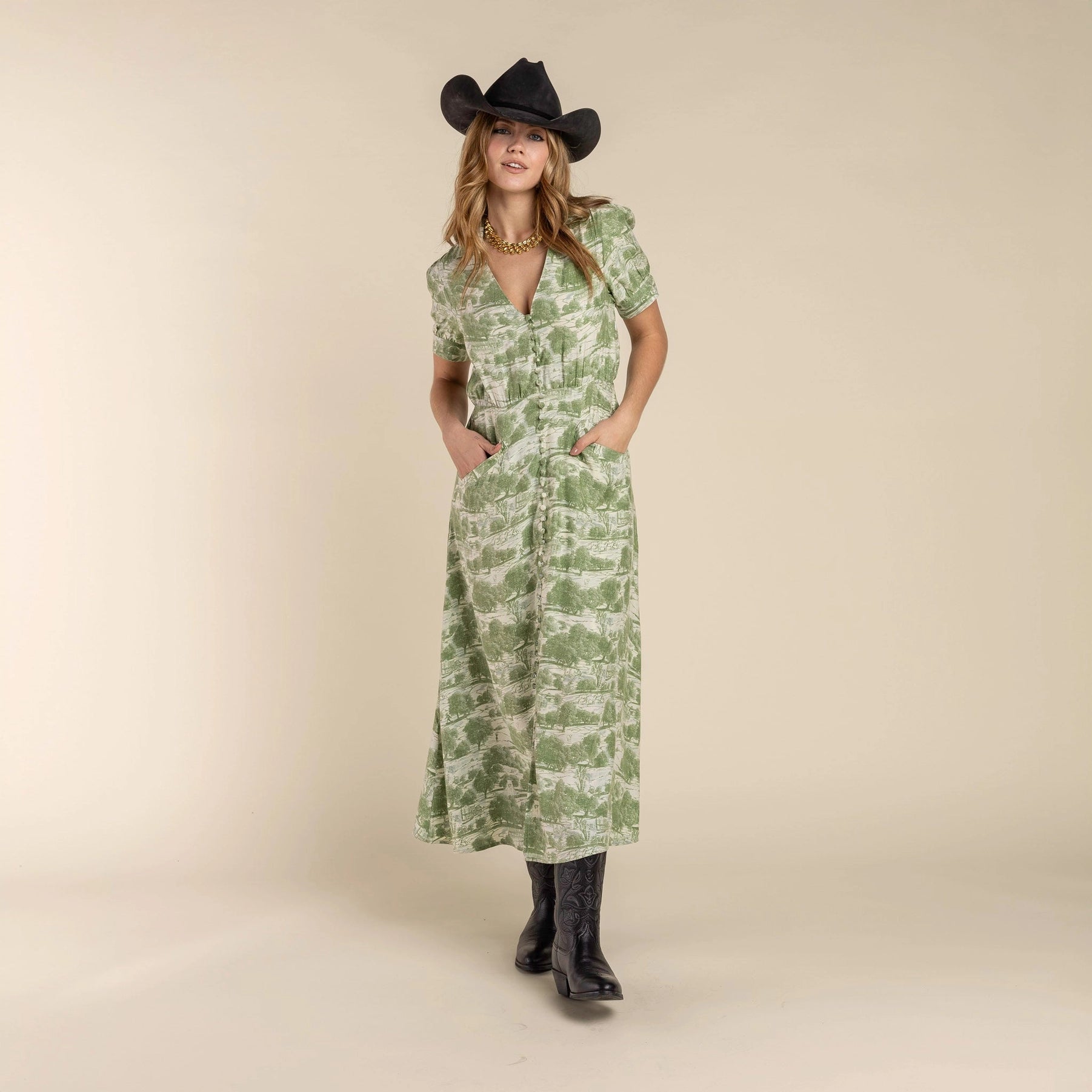 Woman in a green dress holding a black hat against a desert landscape, Woman wearing a green patterned dress and black cowboy hat and the Darcy Dress with feminine charm and a hint of retro style. Stylish dress cowboy rancher girl