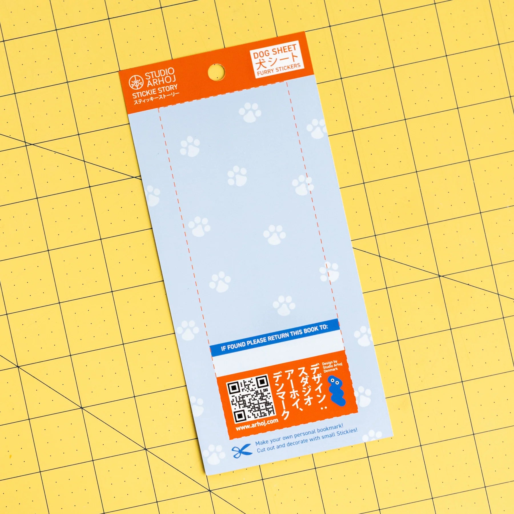 Studio Amo Found Sheet Card Stickers on a yellow grid cutting mat. The sheet is light blue with white paw prints, featuring an orange header and a blue QR code section at the bottom.