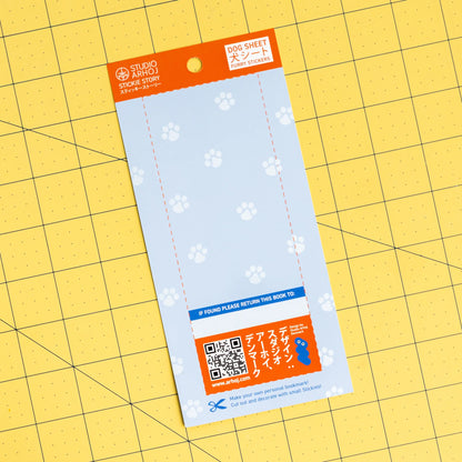 Studio Amo Found Sheet Card Stickers on a yellow grid cutting mat. The sheet is light blue with white paw prints, featuring an orange header and a blue QR code section at the bottom.