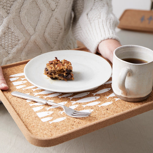 Person holding a tray with a plate of food and a mug on a cork place mat by LIGA which is eco-friendly and features a white firsh pattern.