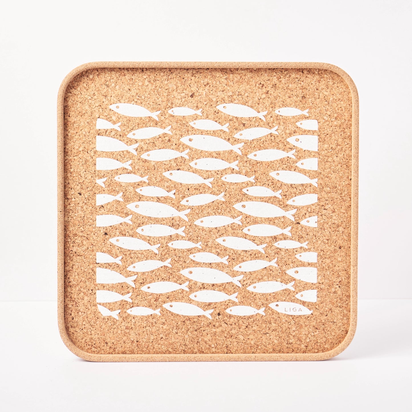 Cork trivet with white fish pattern on a white background