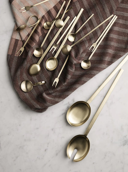Set of gold-colored spoons and forks on a marble surface with a brown cloth underneath.