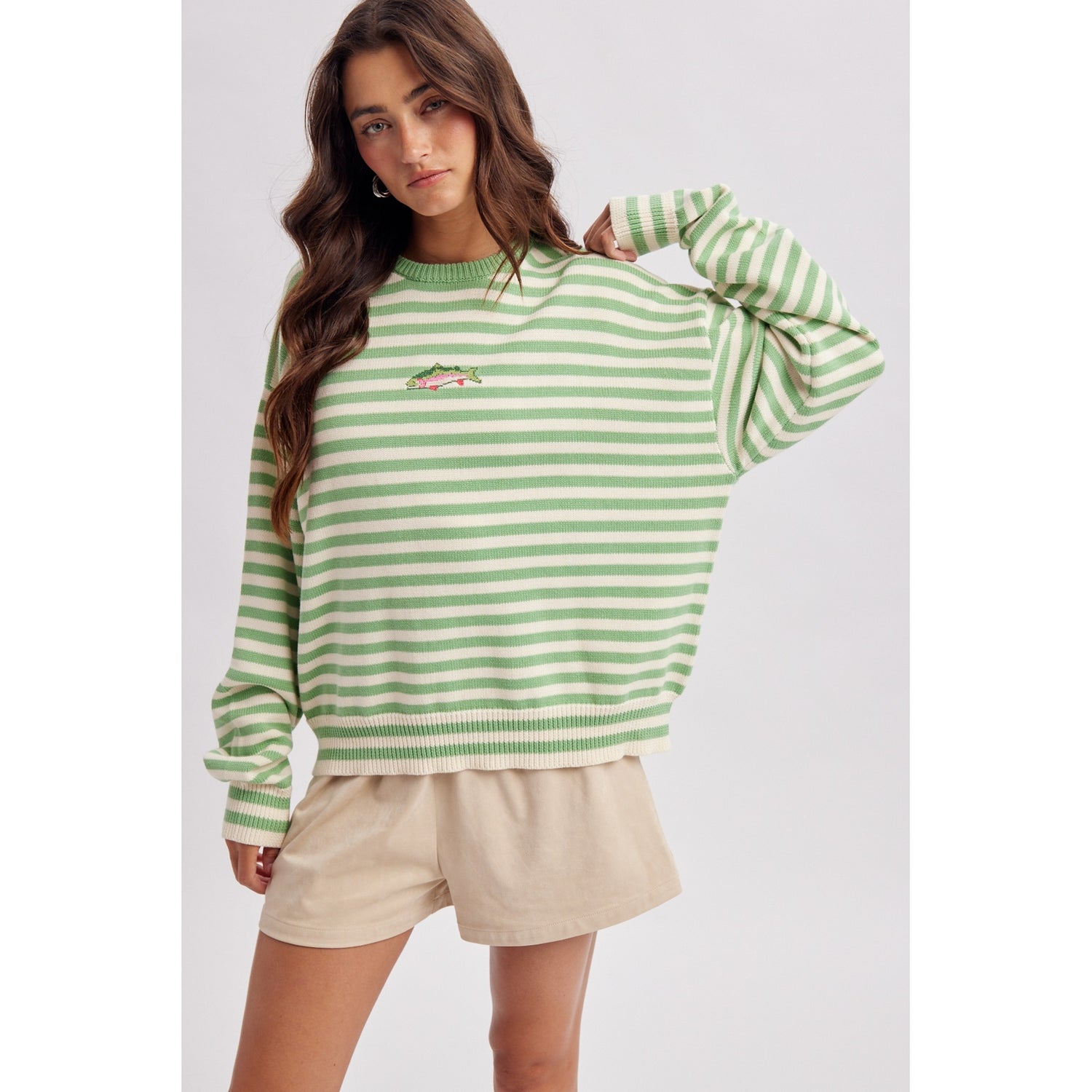 Woman wearing a green and white striped sweater with beige shorts on a light gray background