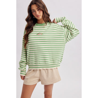 Woman wearing a green and white striped sweater with beige shorts on a light gray background