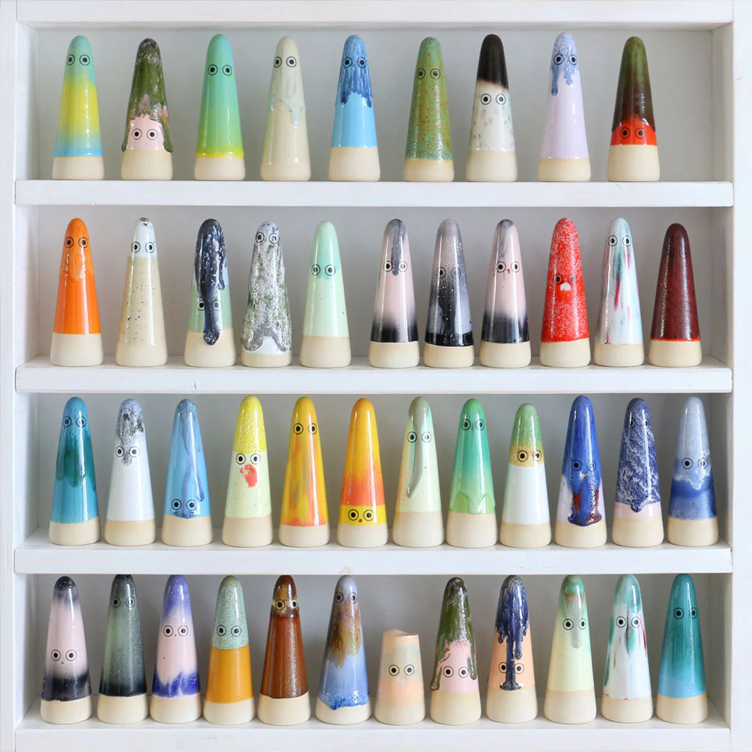 Collection of colorful ceramic figures with faces on a white shelf.