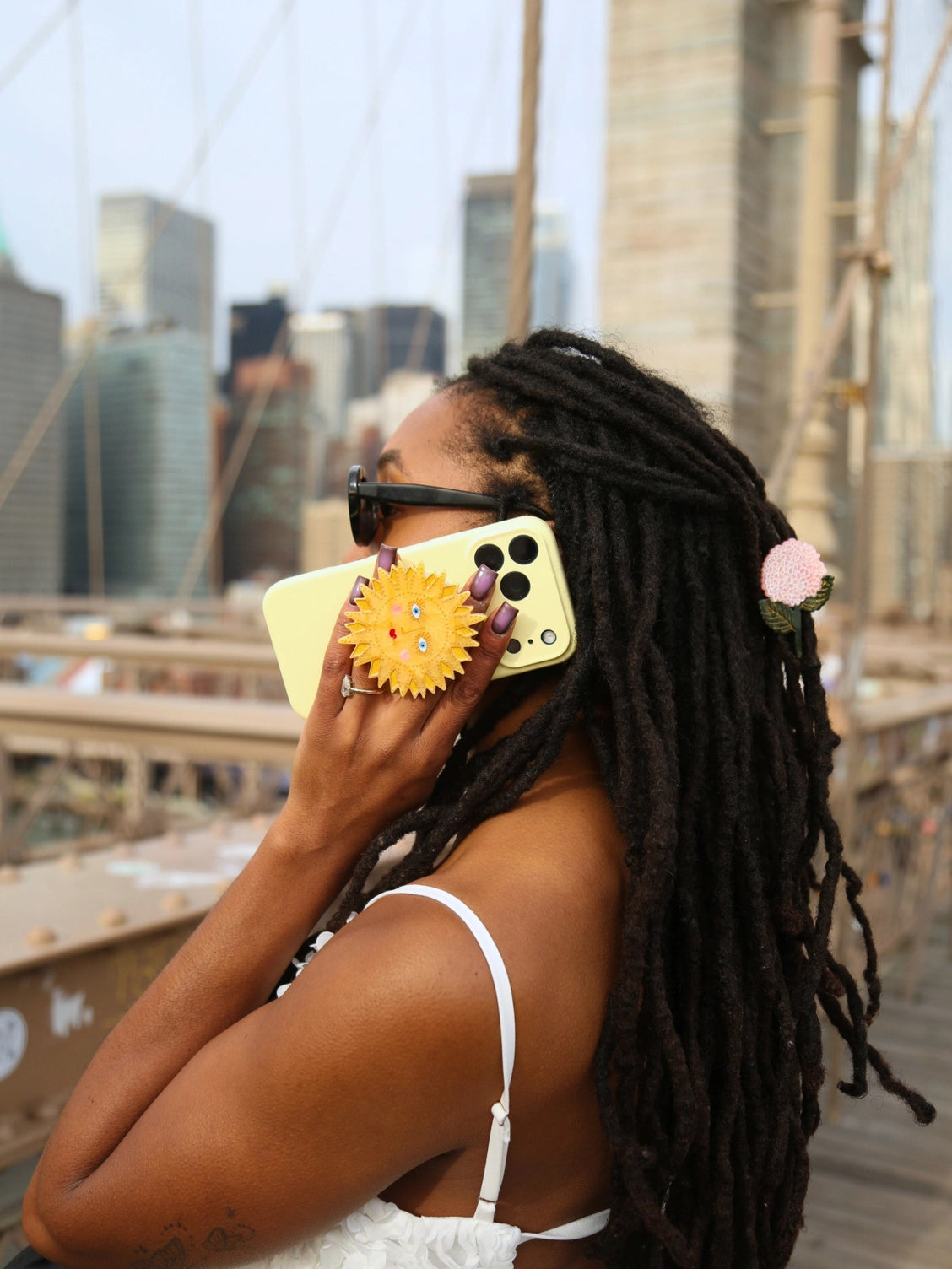 Woman holding a yellow phone case with a sun design, standing on a bridge with city skyline in the background