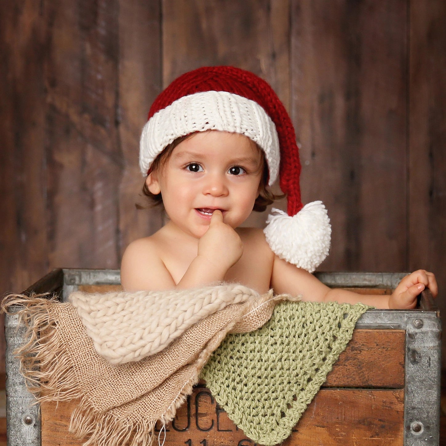 Baby wearing a red and white Santa hat in a wooden crate with a rustic background