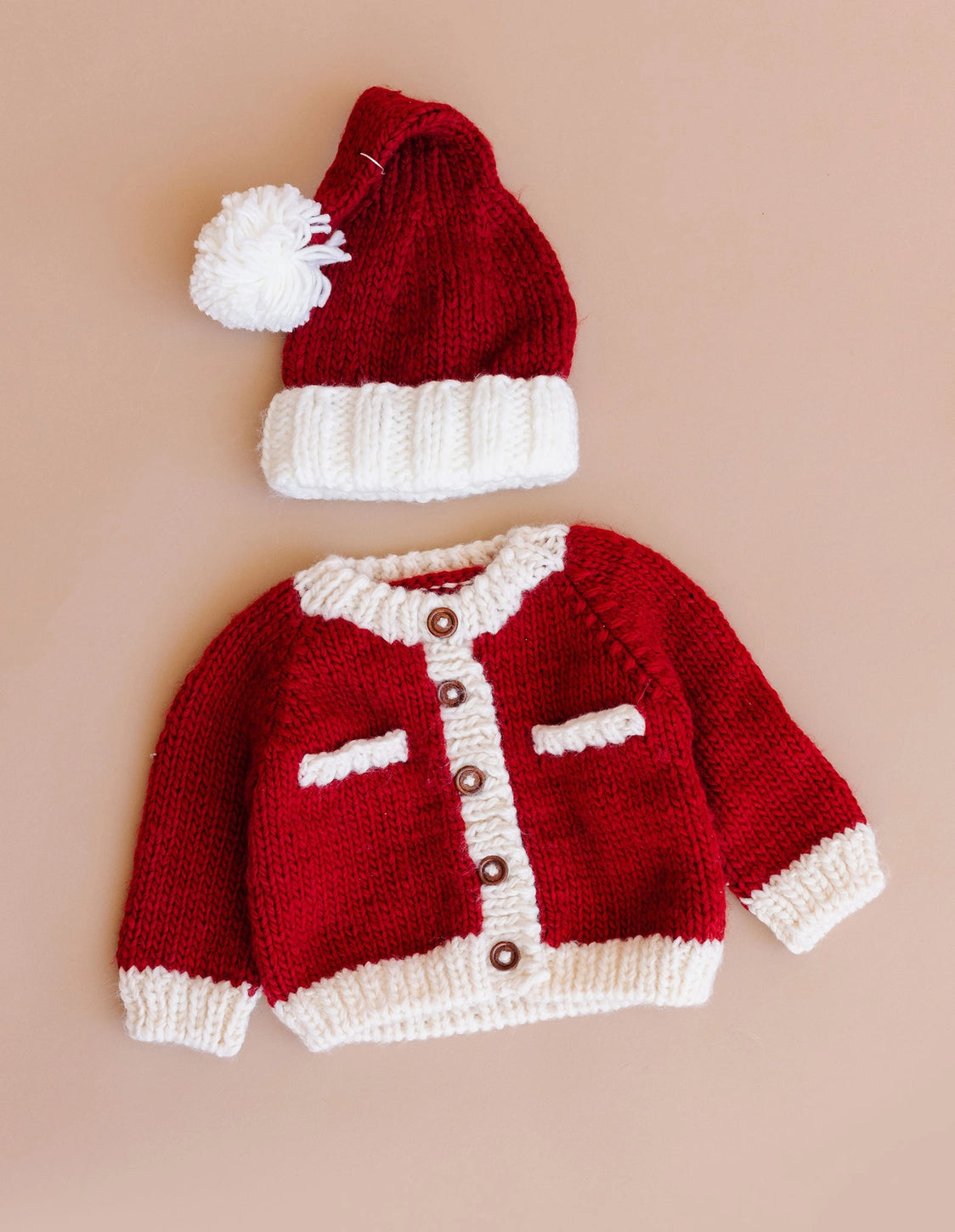 Red knitted baby sweater and hat set on a beige background