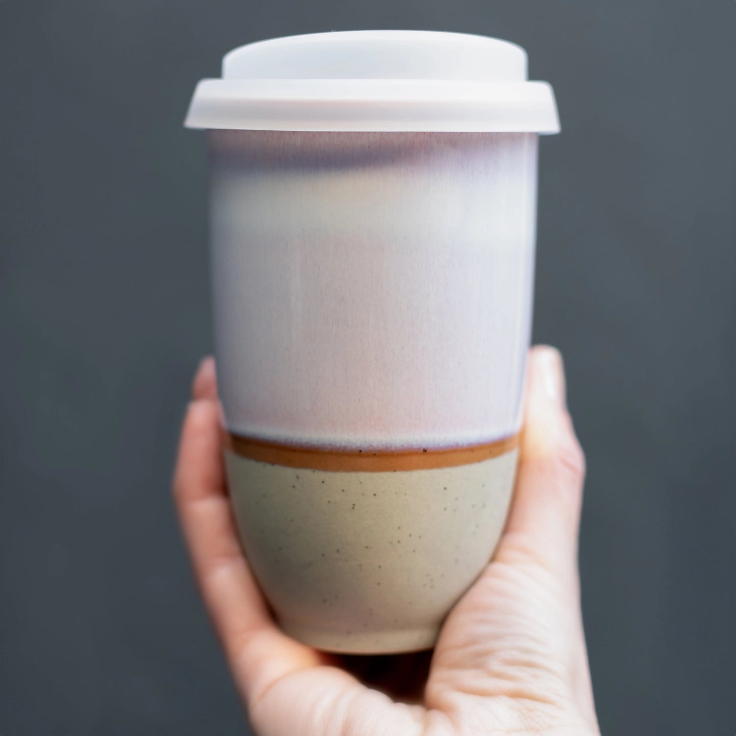Hand holding white and beige glazed ceramic travel mug. Sustainable, reusable