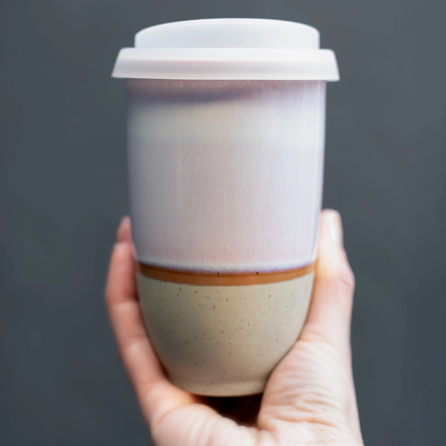 Hand holding white and beige glazed ceramic travel mug. Sustainable, reusable