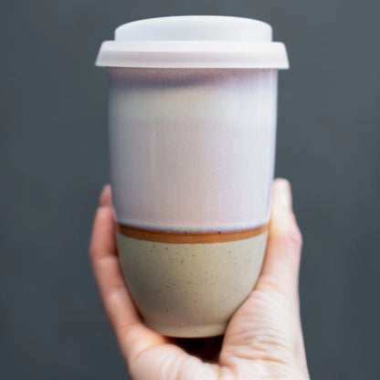 Hand holding white and beige glazed ceramic travel mug. Sustainable, reusable