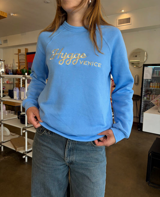 Person wearing a blue sweatshirt with 'Hygge Venice' text in a casual setting.