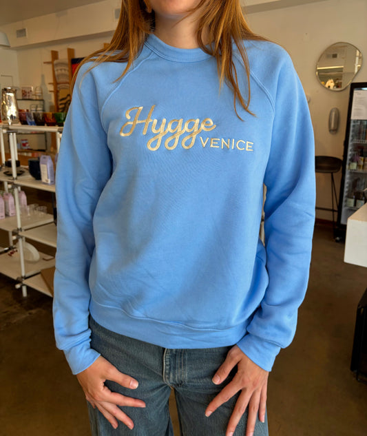 Person wearing a blue sweatshirt with 'Hugge Venice' text in a casual setting