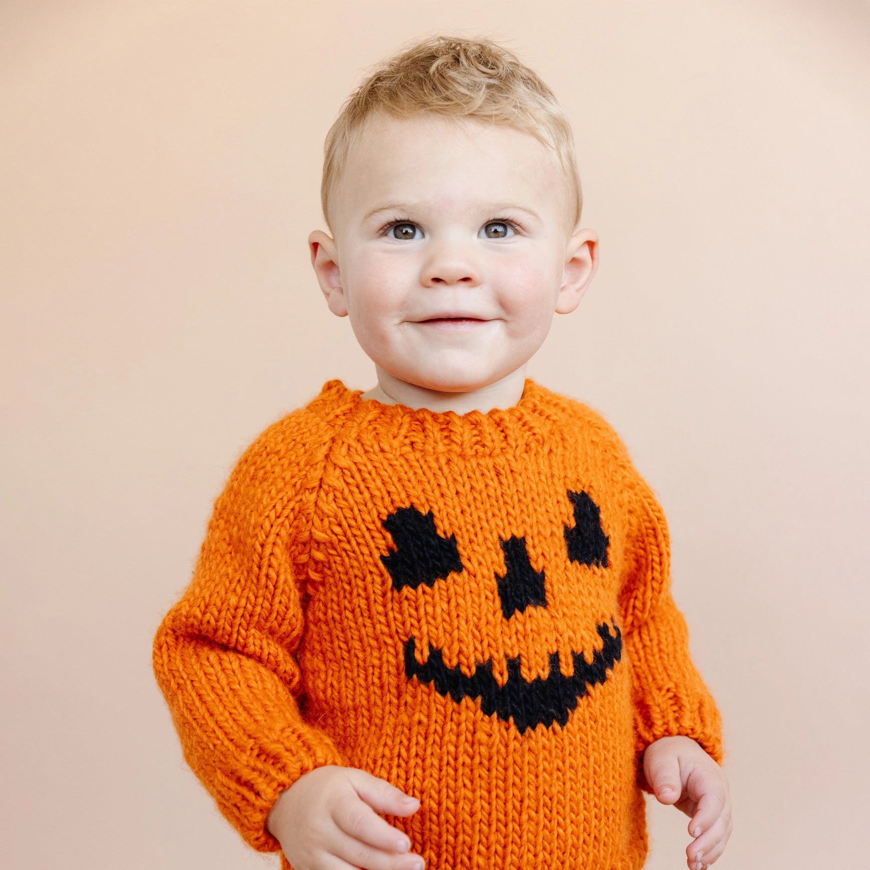 Child wearing an orange sweater with a black pumpkin face design on a beige background